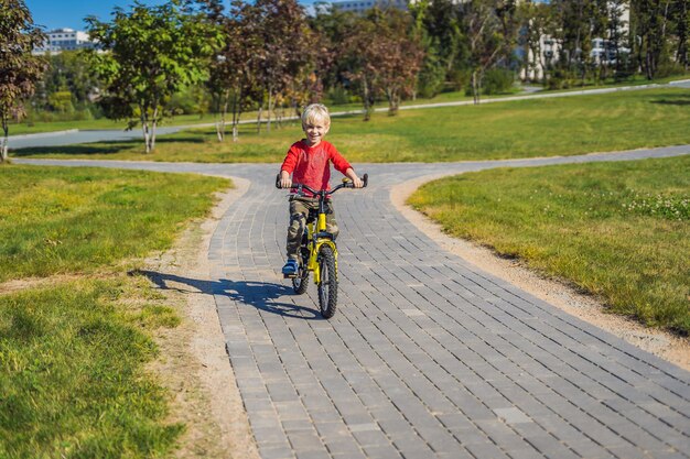 Joyeux garçon de 5 ans s'amusant dans le parc avec un vélo par une belle journée.