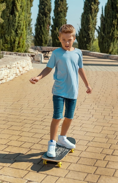 Joyeux garçon d'âge préscolaire en t-shirt apprenant à faire du skateboard dans un parc. Maquette de chemise