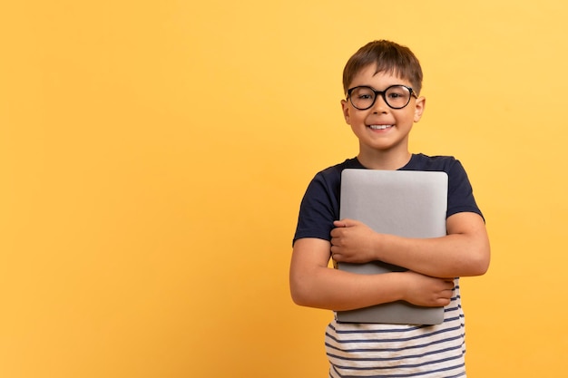 Joyeux garçon d'âge scolaire embrassant un ordinateur portable