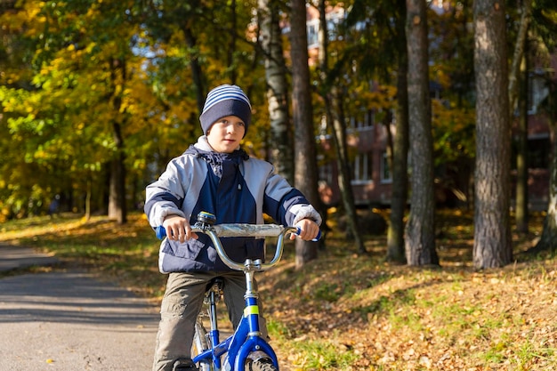 Un joyeux garçon de cinq ans fait du vélo dans un chapeau et une veste d'automne