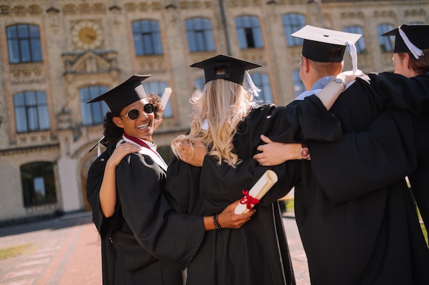 Joyeux garçon portant des lunettes de soleil serrant ses camarades de groupe après leur diplôme dans la cour de l'université