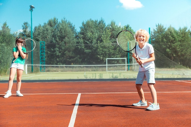 Joyeux garçon se sentant heureux de jouer au tennis avec une fille