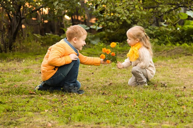 Joyeux garçon souriant en veste jaune présente un bouquet de fleurs à une petite fille en écharpe jaune