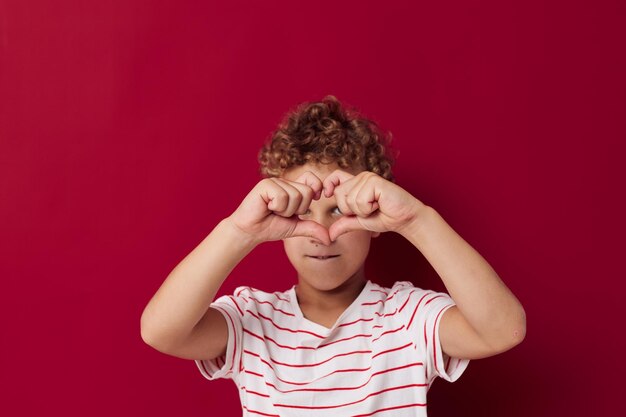 Joyeux garçon en t-shirt rayé sourire posant sur fond rouge