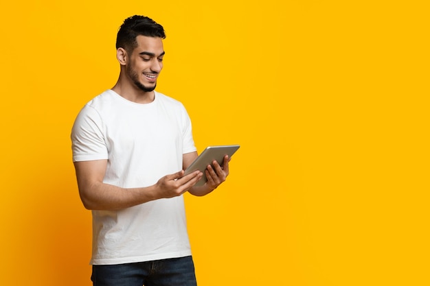 Photo joyeux gars arabe à l'aide d'une tablette numérique fond de studio jaune