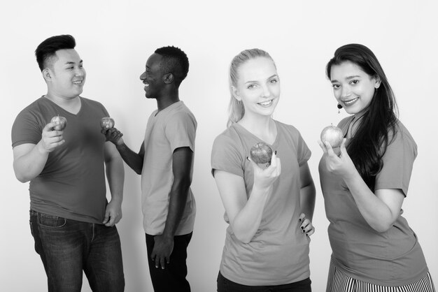 Joyeux groupe diversifié d'amis multiethniques souriant tout en tenant une pomme rouge et posant avec des amis parlant dans le dos