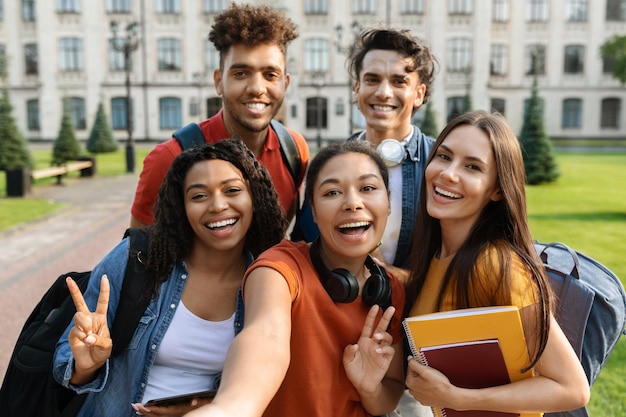 Joyeux groupe multiethnique d'étudiants faisant ensemble un selfie à l'extérieur