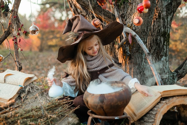 Joyeux Halloween. Une jolie fille en costume de sorcière est dans l'antre de la sorcière. Jolie petite sorcière gaie prépare une potion magique. Halloween.