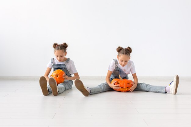 Joyeux Halloween, vacances et concept d'enfance - Jolies petites sœurs jumelles avec une citrouille Jack-o'-lantern s'amusant tout en passant du temps à l'intérieur