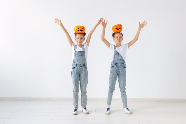 Joyeux Halloween, vacances et concept d'enfance - Jolies petites sœurs jumelles avec une citrouille Jack-o'-lantern s'amusant tout en passant du temps à l'intérieur