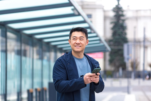 Joyeux et heureux asiatique utilisant un téléphone souriant et regardant la caméra près de l'homme d'affaires de l'aéroport en voyage touristique