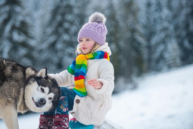 Joyeux hiver enfant fille chien husky avec enfant dans la neige sur fond de forêt d'hiver