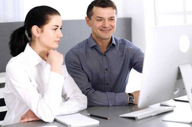 Joyeux homme d'affaires souriant et femme travaillant avec un ordinateur dans un bureau moderne. Headshot lors d'une réunion ou d'un lieu de travail. Travail d'équipe, partenariat et concept d'entreprise.