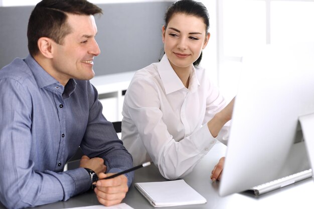 Joyeux homme d'affaires souriant et femme travaillant avec un ordinateur dans un bureau moderne. Headshot lors d'une réunion ou d'un lieu de travail. Travail d'équipe, partenariat et concept d'entreprise.