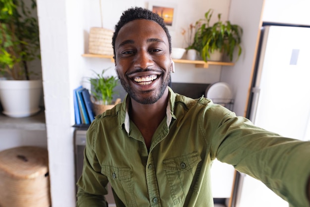 Photo joyeux homme afro-américain assis à table dans la cuisine, ayant un appel vidéo. passer du temps de qualité seul à la maison.