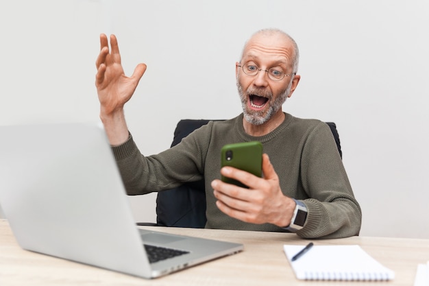 Joyeux homme âgé sur le lieu de travail tenant un téléphone portable dans ses mains
