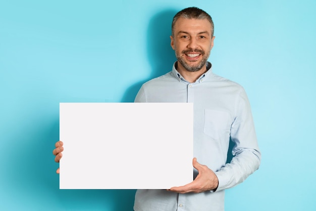 Joyeux homme d'âge moyen tenant un fond bleu d'affiche de papier vierge