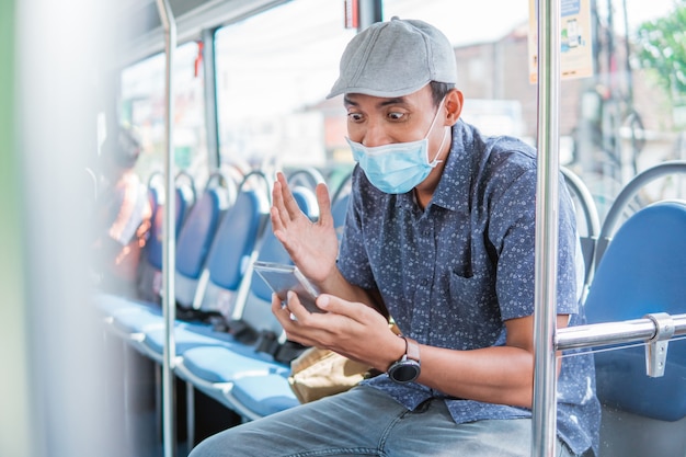 Joyeux homme asiatique acclamant la célébration en regardant un smartphone dans un bus public avec un masque