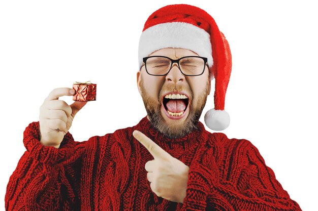 Joyeux homme barbu en bonnet de Noel, lunettes et pull en laine rouge détient un petit cadeau de Noël isolé sur fond blanc, Noël ou design du nouvel an