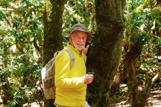 Joyeux homme barbu senior avec sac à dos et casquette de randonnée dans la forêt bénéficiant d'un mode de vie sain et de la retraite