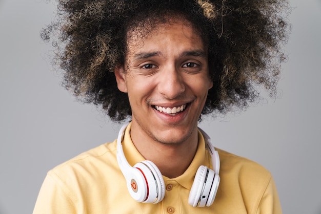 joyeux homme caucasien avec une coiffure afro portant des écouteurs souriant isolé sur un mur gris