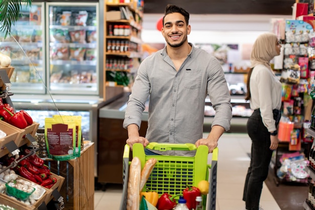 Joyeux homme égyptien faisant des courses à pied dans un supermarché moderne