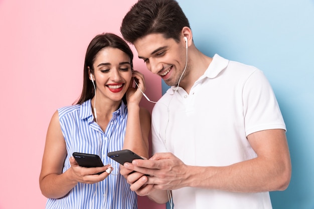 joyeux homme et femme portant des écouteurs et à l'aide de téléphones portables, isolés sur un mur coloré