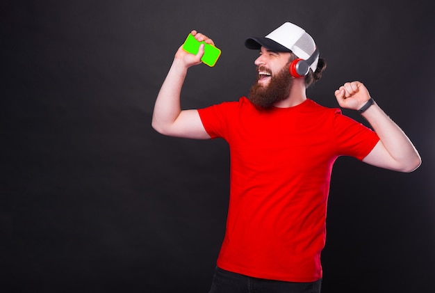 Joyeux homme hipster barbu en t-shirt rouge, écouter de la musique au casque sans fil