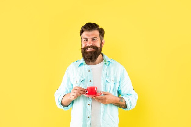 Joyeux homme mal rasé en chemise avec café sur fond jaune matin