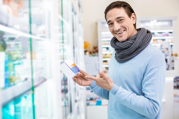 Joyeux homme vigoureux portant un foulard tout en tenant des médicaments pour soulager les symptômes du rhume