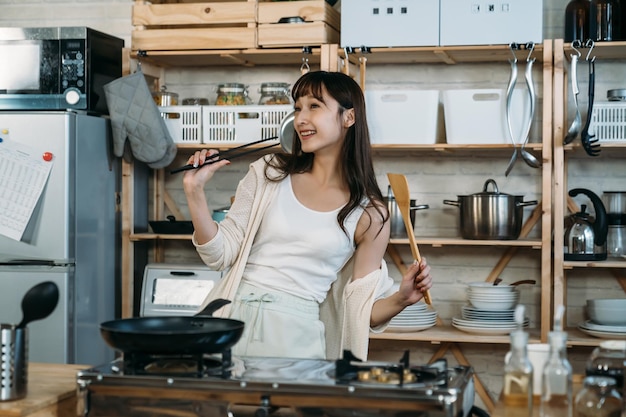 Joyeux japonais asiatique tenant la baguette et la spatule dansant dans la cuisine, profitez de la matinée de détente.