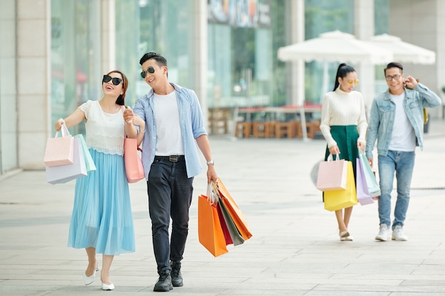 Joyeux jeune couple asiatique heureux marchant dans la rue avec des sacs en papier après le shopping