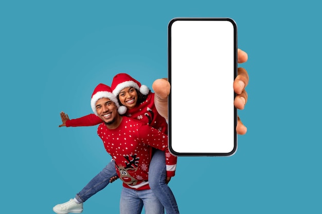 Joyeux jeune couple noir montrant un téléphone portable à écran vide