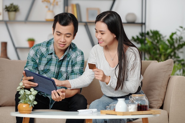 Joyeux jeune couple vietnamien avec carte de crédit et tablette numérique effectuant des achats en ligne