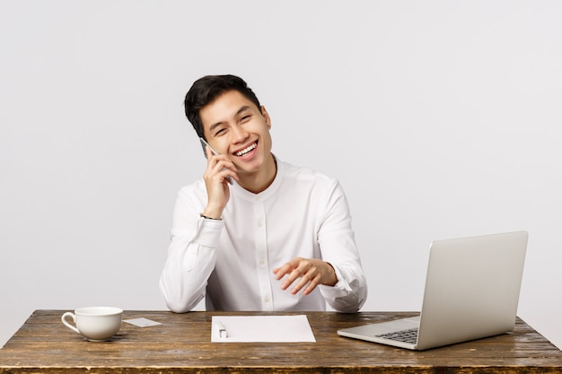 Joyeux jeune entrepreneur asiatique souriant, parler au téléphone au bureau