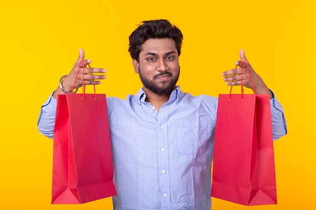 Joyeux jeune hipster tient des sacs à provisions rouges sur un mur jaune. Le concept de shopping dans le supermarché et cadeaux.
