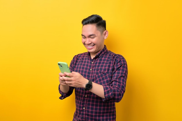 Joyeux jeune homme asiatique utilisant un smartphone pour envoyer des messages avec des amis isolés sur fond jaune