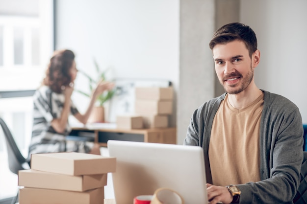 Joyeux jeune homme assis devant son ordinateur portable au bureau