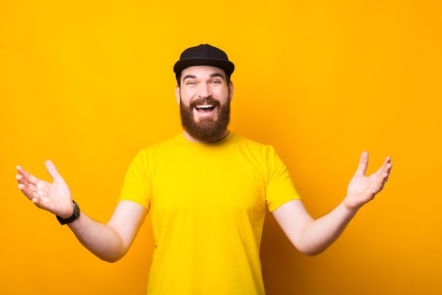 Photo joyeux jeune homme barbu faisant un geste de bienvenue sur jaune, ravi de vous rencontrer