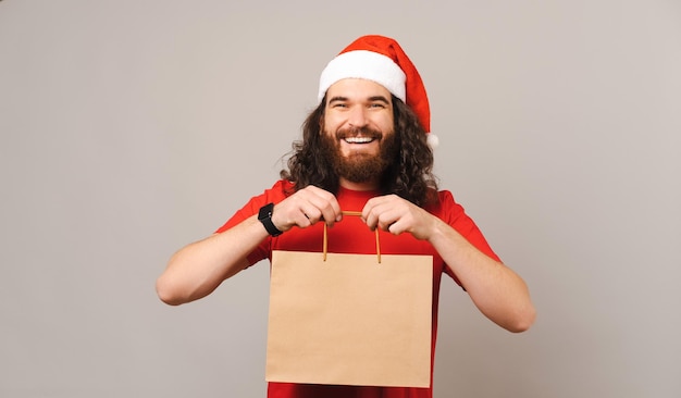 Joyeux jeune homme barbu portant un chapeau de Noël tient un sac en papier