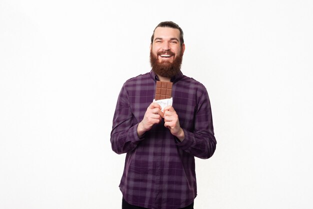 Joyeux jeune homme en chemise à carreaux tenant une barre de chocolat et souriant