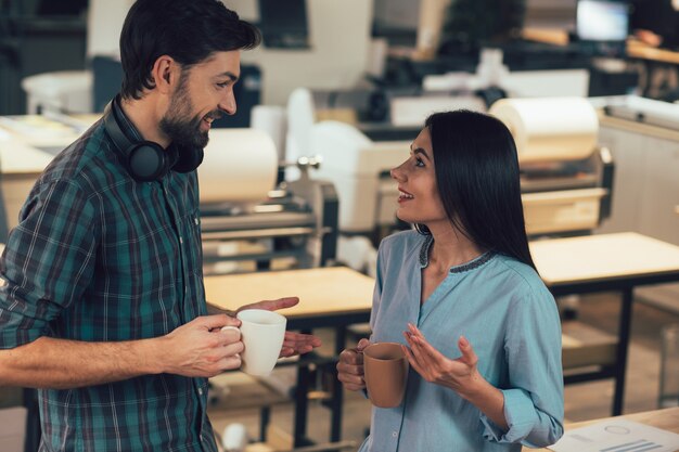 Joyeux jeune homme et femme dans une maison d'édition debout avec des tasses et parlant