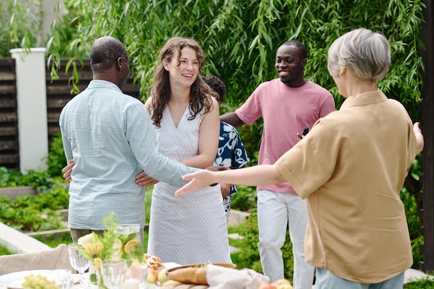 Joyeux jeune homme et femme saluant les parents interculturels avec des câlins et leur disant bonjour lors d'une visite à un couple d'âge mûr le week-end