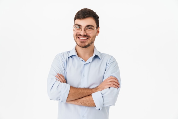 joyeux jeune homme à lunettes posant avec les mains croisées et souriant isolé sur mur blanc