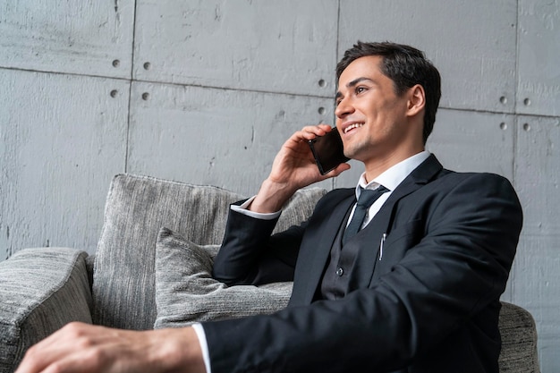 Joyeux jeune homme parlant au téléphone dans un fauteuil