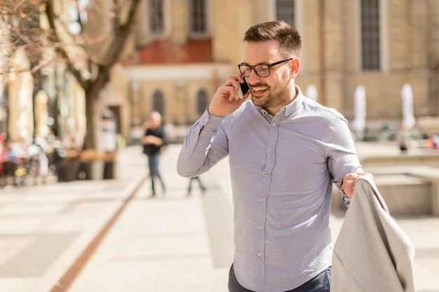 Joyeux jeune homme utilise un téléphone portable dans la rue