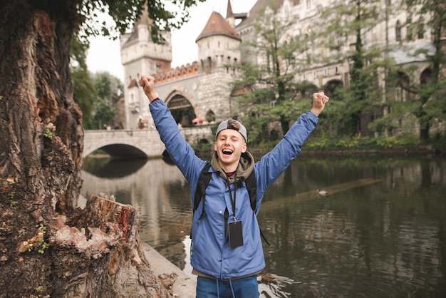 Joyeux jeune touriste se réjouit avec ses mains levées sur le château de Vajdahunyad,