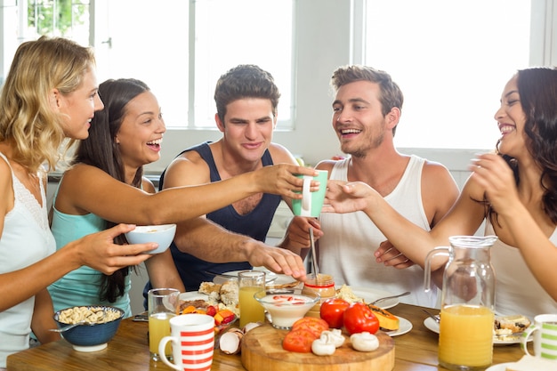 Joyeux jeunes amis prenant son petit déjeuner à table dans la maison