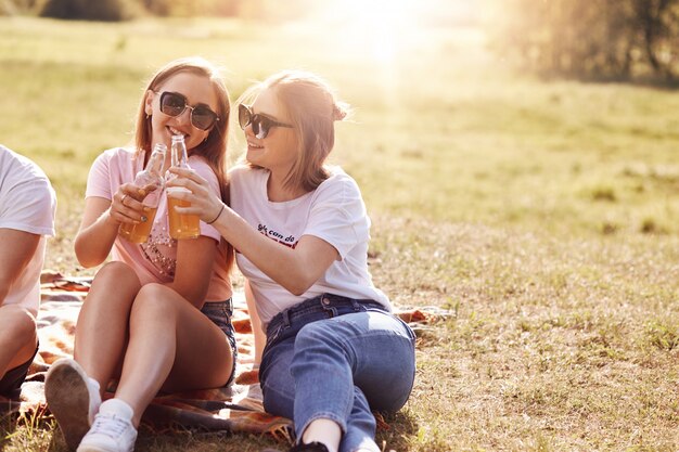 Joyeux jeunes compagnes féminines tintent des bouteilles de boisson énergisante