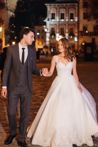 De joyeux jeunes mariés marchent en se tenant la main dans l'ancienne rue de la ville européenne